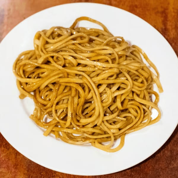 A white plate filled with August Moon's glistening, golden-brown lo mein noodles.