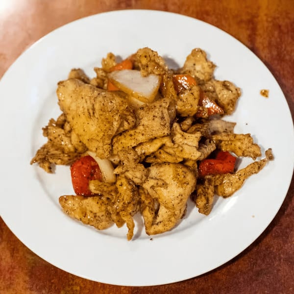 August Moon's Chinese black pepper chicken with red peppers and onions on a white plate.